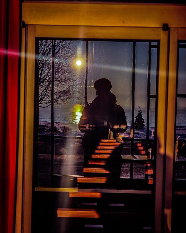 A silhouetted figure reflected in a window overlooking the lake.