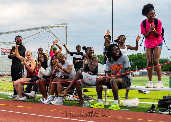 Spectators cheer from a bench beside the track.